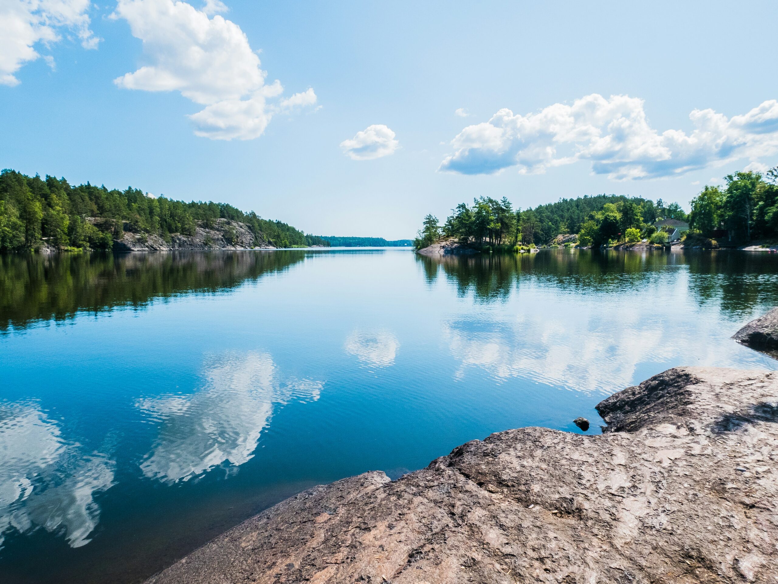 Spegelblank sjö som reflekterar himmel och moln en sommardag