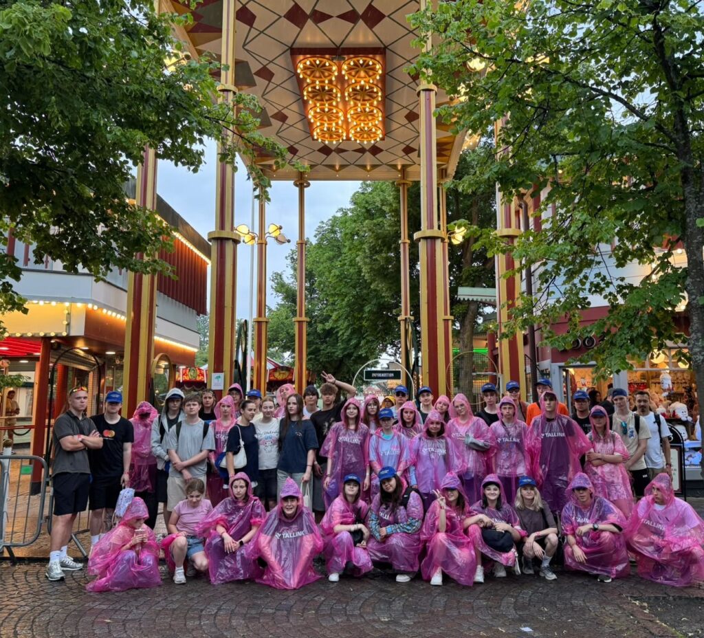 Ungdomar i rosa regnrockar under en portal på Gröna lund
