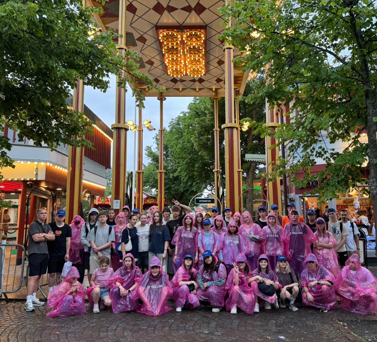 Ungdomar i rosa regnrockar under en portal på Gröna lund